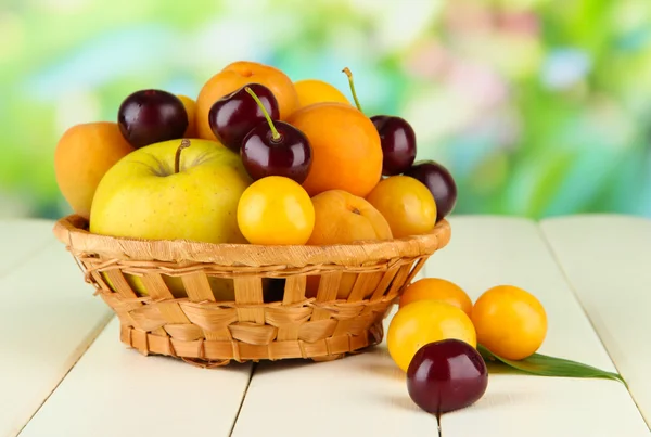 Φωτεινό καλοκαιρινά φρούτα στο καλάθι στο ξύλινο τραπέζι στο φυσικό περιβάλλον — Φωτογραφία Αρχείου