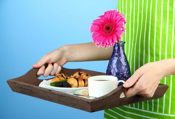 Woman in green apron holding wooden tray with breakfast, on color background — Stock Photo, Image