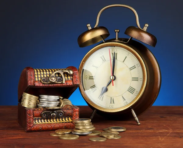 Antieke clock en munten op houten tafel op donkere kleur achtergrond — Stockfoto