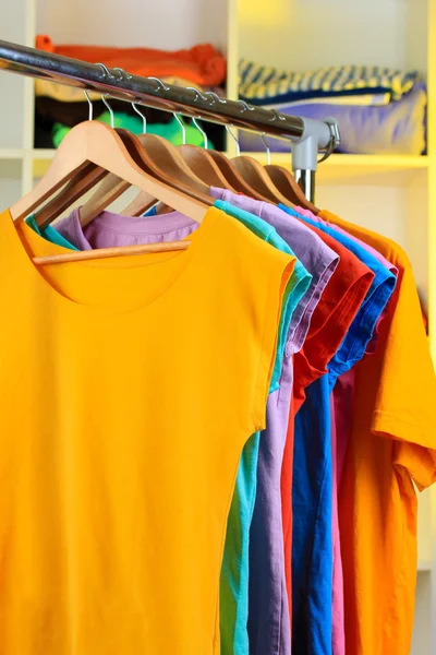 Variety of casual t-shirts on wooden hangers on shelves background — Stock Photo, Image