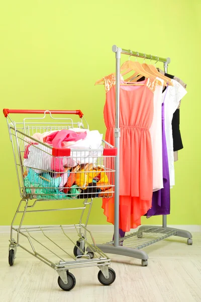 Elbiseler, renkli duvar arka plan üzerinde alışveriş sepeti — Stok fotoğraf