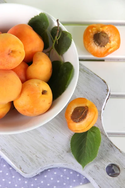 Apricots in plate on board on napkin on wooden table — Stock Photo, Image