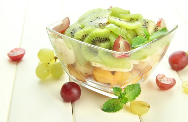 Smakelijke fruitsalade in glazen kom, op witte houten tafel — Stockfoto