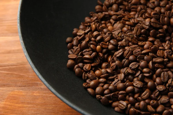 Black wok pan with coffee beans on wooden table, close up — Stock Photo, Image