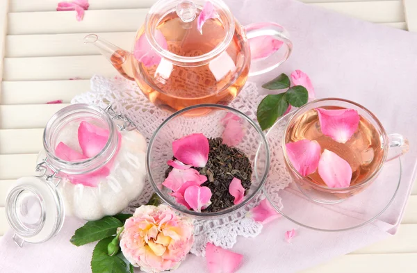 Konvice a šálek čaje z tea rose na ubrousek na dřevěné pozadí — Stock fotografie
