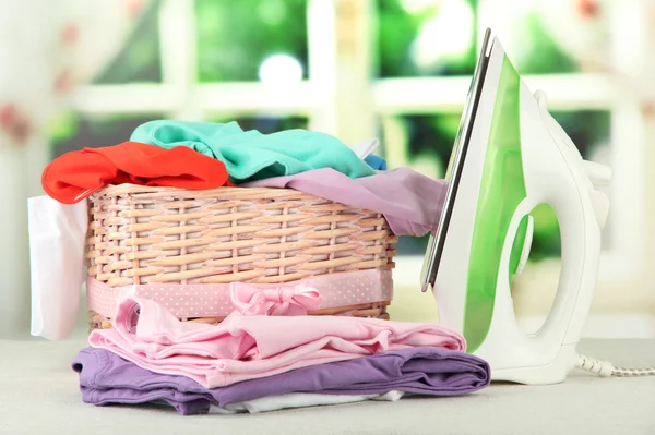 Steam iron and wicker basket with clothes, on bright background — Stock Photo, Image