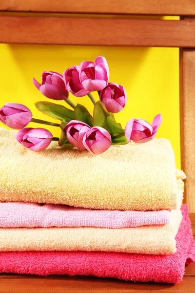 Handdoeken en bloemen op houten stoel op gele achtergrond — Stockfoto