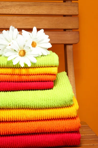 Πετσέτες και λουλούδια σε ξύλινη καρέκλα σε πορτοκαλί φόντο — Φωτογραφία Αρχείου