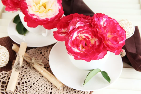 Roses in cups on napkins on wooden background — Stock Photo, Image