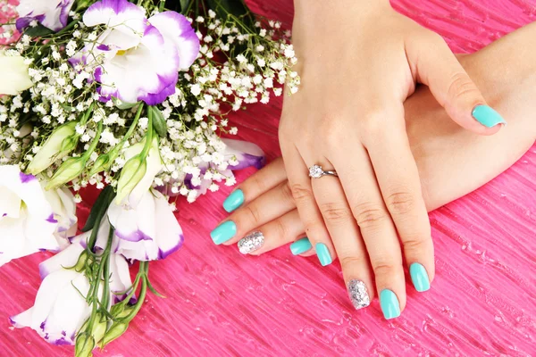 Mooie vrouw handen met blauwe manicure in de buurt van boeket van mooie bloemen, op een achtergrond met kleur — Stockfoto
