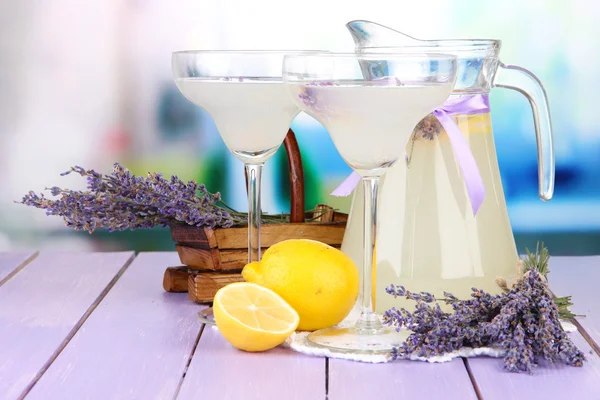 Lavender lemonade in glass jug and cocktail glasses, on bright background — Stock Photo, Image