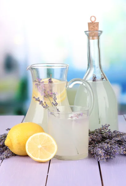 Lavendellimonade in Glasflasche und Krug, auf violettem Holztisch, auf hellem Hintergrund — Stockfoto