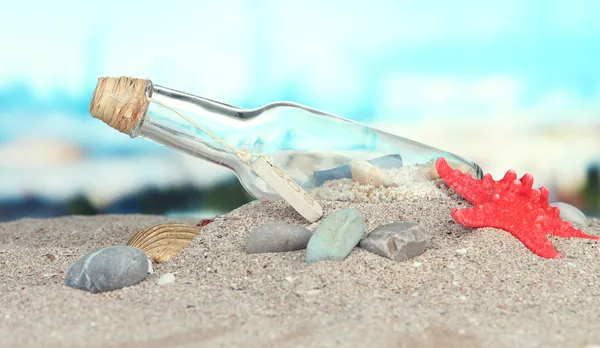 Glazen fles met opmerking binnen op heldere blauwe achtergrond — Stockfoto