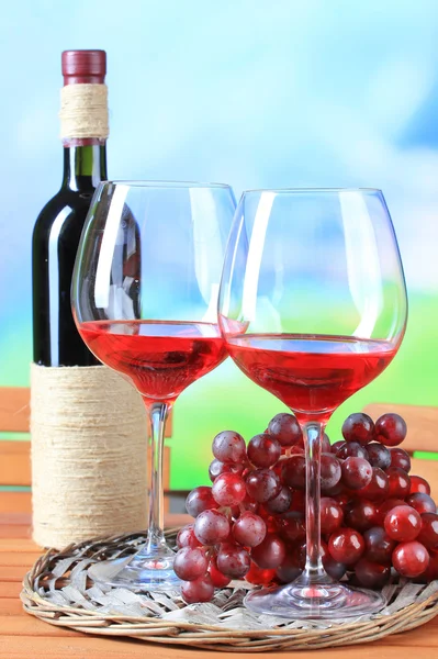 Glazen wijn op gevlochten lade op houten tafel op aard achtergrond — Stockfoto