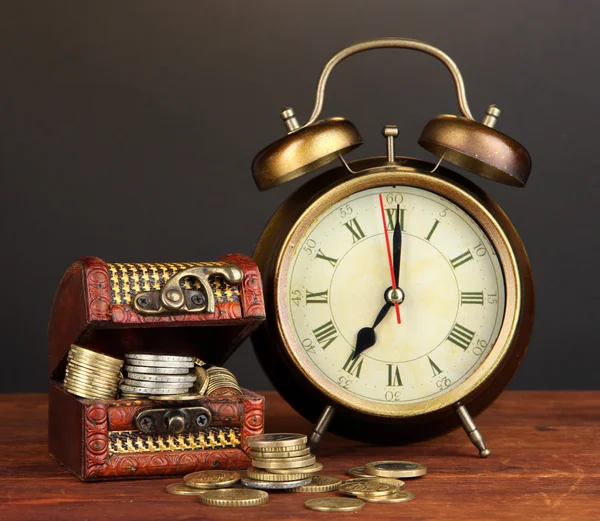 Antieke clock en munten op houten tafel op zwarte achtergrond — Stockfoto