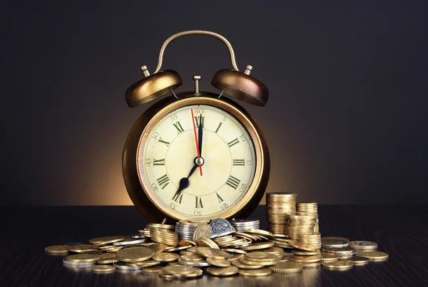 Antieke clock en munten op houten tafel op zwarte achtergrond — Stockfoto