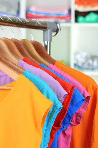 Variety of casual t-shirts on wooden hangers on shelves background — Stock Photo, Image