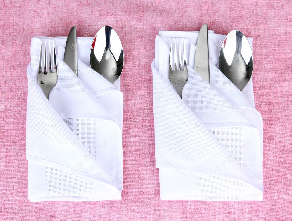 Folded napkin with fork, spoon and knife on color background