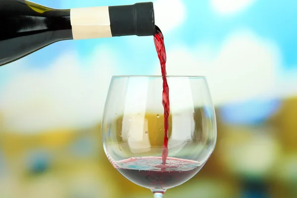 Czerwone wino jest wlewa kieliszek do wina, na jasnym tle — Zdjęcie stockowe