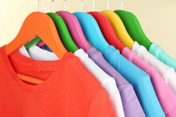 Verschillende shirts op kleurrijke hangers op beige achtergrond — Stockfoto