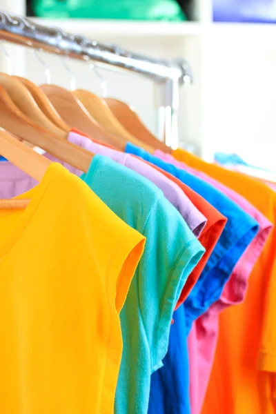 Verscheidenheid van casual t-shirts op houten hangers op planken achtergrond — Stockfoto