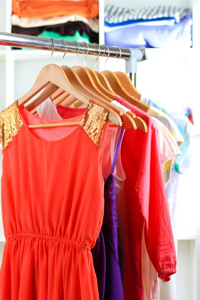 Verscheidenheid van kleding op houten hangers op planken achtergrond — Stockfoto