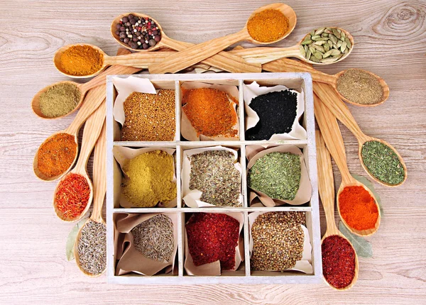 Assortment of spices in wooden spoons and box, on wooden background — Stock Photo, Image