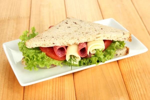 Sanduíche saboroso com salsicha de salame e legumes na placa branca, no fundo de madeira — Fotografia de Stock