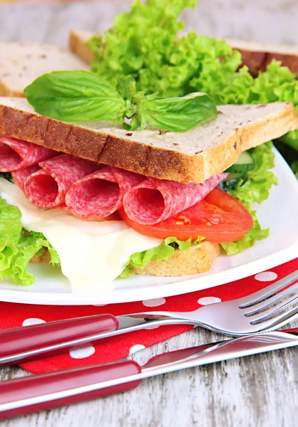 Komposition med fruktjuice och god smörgås med salami korv och grönsaker på färg Servett, på träbord bakgrund — Stockfoto