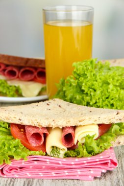 Lezzetli sandviç salam sosis ve parlak zemin üzerine ahşap masa üzerinde renkli peçete üzerinde sebze ve meyve suyu ile kompozisyon