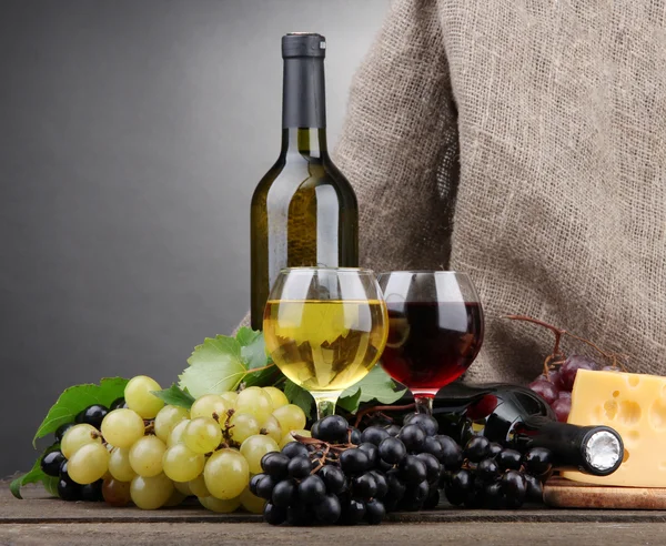 Bottles and glasses of wine, cheese and grapes on grey background — Stock Photo, Image