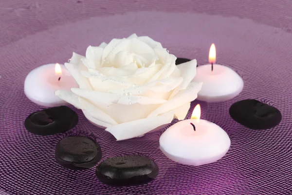 Piedras de spa con flores y velas en agua en el plato —  Fotos de Stock