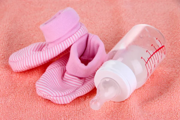 Bottle for milk and booties on pink towel background — Stock Photo, Image