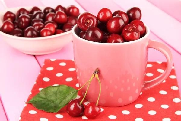 Cherry berries in cup and bowl on wooden table close-up — Stock Photo, Image