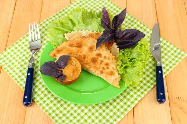 Gustosi chebureks con erbe fresche su piatto, su fondo di legno — Foto Stock