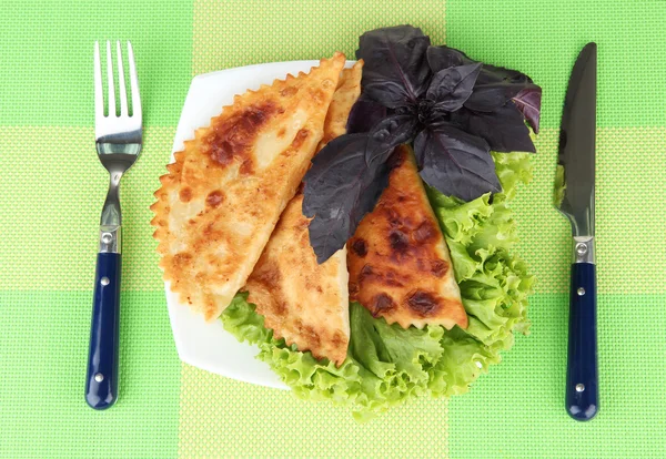 Gustosi chebureks con erbe fresche sul piatto, su sfondo tovagliolo di colore — Foto Stock