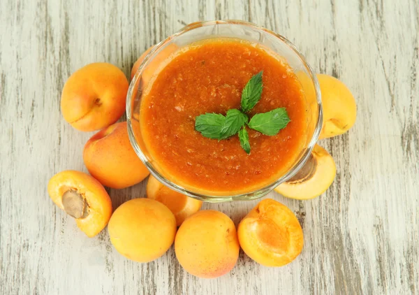 Apricot jam in glass bowl and fresh apricots, on wooden background — Stock Photo, Image