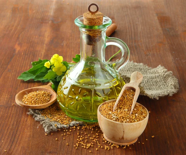 Jar of mustard oil and seeds with mustard flower on wooden background — Stock Photo, Image