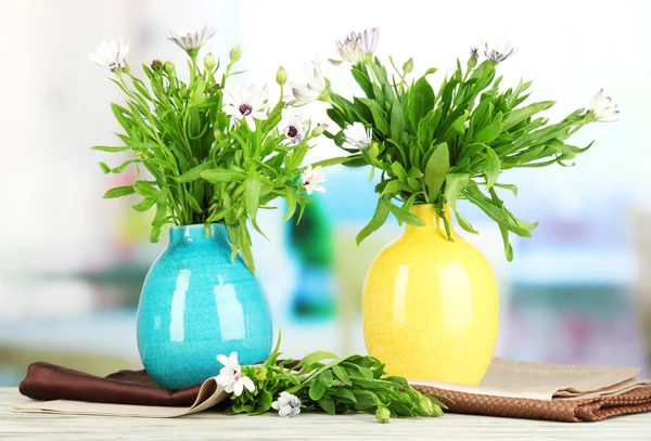 Bouquet of beautiful summer flowers in color vases, on wooden table , on bright background — Stock Photo, Image