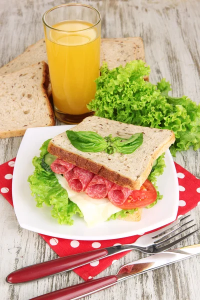 フルーツ ジュース、サラミ ソーセージと野菜の木製のテーブルの背景の色のナプキンにおいしいサンドイッチのコンポジション — ストック写真