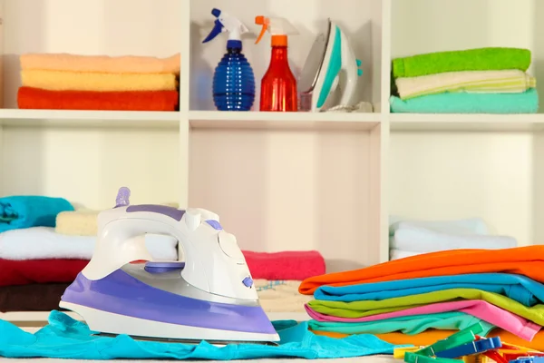 Clothes and iron on table on shelves background — Stock Photo, Image