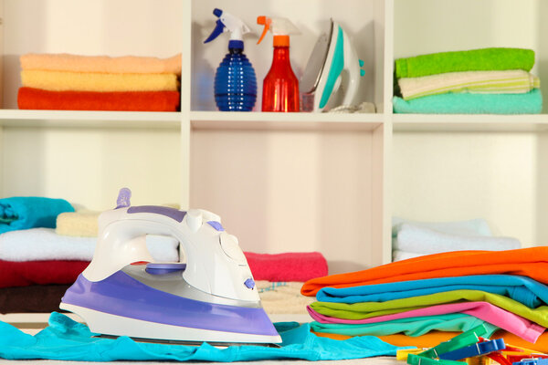 Одежда и утюг на столе на полках
