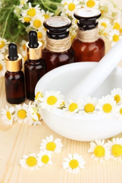 Aceite esencial y flores de manzanilla en mortero sobre mesa de madera —  Fotos de Stock