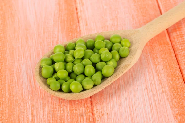 Sweet green peas in spoon on wooden background — Stock Photo, Image