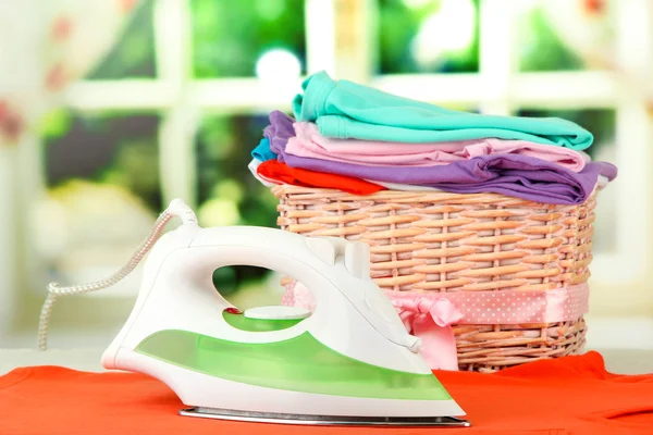 Dampfbügeleisen und Weidenkorb mit Kleidung, auf hellem Hintergrund — Stockfoto