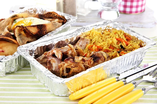 Food in boxes of foil on tablecloth — Stock Photo, Image