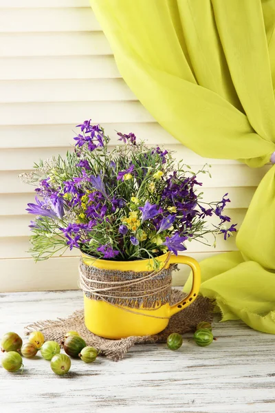 Mooi boeket van wilde bloemen in cup en bessen op houten tafel — Stockfoto