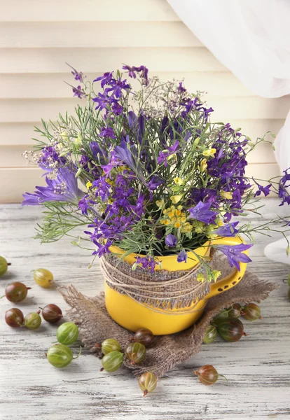 Vacker bukett av blommor i kopp och bär på träbord — Stockfoto