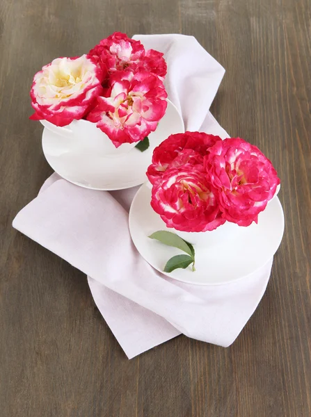 Roses in cups on napkin on wooden background — Stock Photo, Image