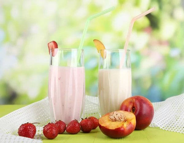 Leckere Milchshakes mit Erdbeeren und Pfirsich auf Holztisch vor natürlichem Hintergrund — Stockfoto